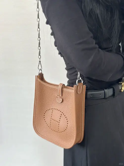Profile View: Gold Hermes Evelyne Replica Styling Side view of gold Evelyne TPM replica bag worn crossbody with jeans