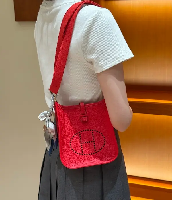 Styling the Rouge H Hermes Evelyne TPM Replica Model wearing bright red Evelyne 16 replica bag crossbody with dress