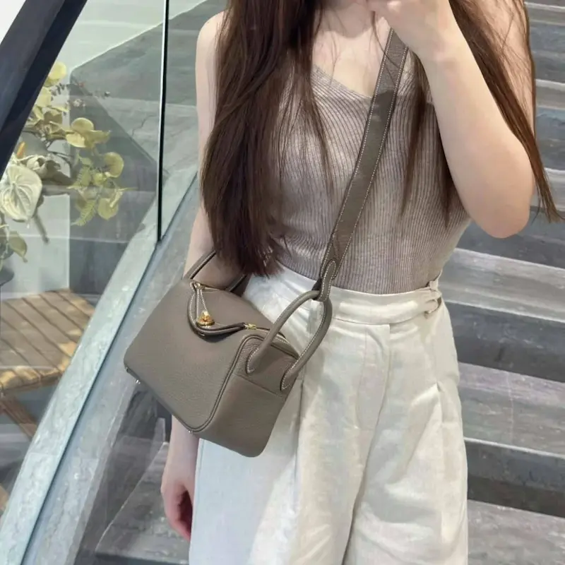 Replica Lindy 19 in Etoupe carried crossbody Woman wearing replica Hermes Lindy 19 in Etoupe gray crossbody style